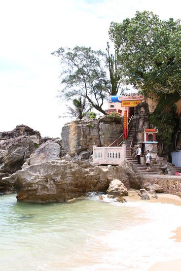 Ein kleiner Tempel mit Leuchtturm auf einen kleinen Felsen vorm Strand gebaut.