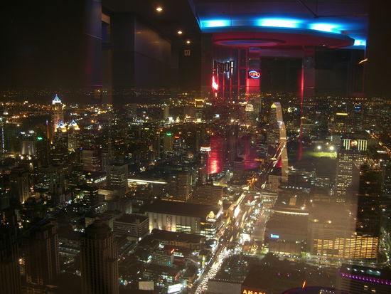 Auf der Thannon Ratchadamri staut sich der Feierabendverkehr. Im Hintergrund spiegeln sich die Neonlichter der Skylounge, in der wir bei einem Cocktail die Aussicht genießen.