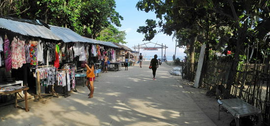 Ein sandiger Pfad, an dem sich Verkaufsbuden aneinanderreihen, führt zum Strand.