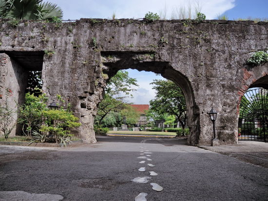 hinter dem Tor ist eine zweite Mauer sichtbar, die von einem Rundbogen durchbrochen ist. In der Mitte die Fußspuren Rizal als er seinem letzten Gang zur Hinrichtungsstätte antrat.