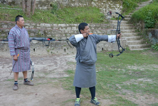 Im Schatten des Dzong trainieren Bhutaner im traditionellen Gewand den Nationalsport des Landes mit nicht ganz so tradionellen Sportbögen. Man verlässt sich sehr auf die Treffsicherheit der Schützen, denn in etwa 100m Entfernung stehen andere Männer und lassen eine ca. 2 - 3 m breite Gasse zum Ziel