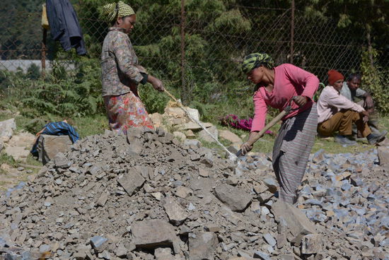 Zwei Frauen, eine Schaufel: Füllmaterial wird auf der neue Trasse verteilt, wobei die eine Arbeiterin mit einem Seil an der schweren Schaufel zieht