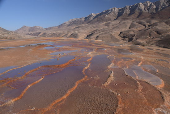 Schillernde Farben der Ablagerungen vor Bergkulisse bei strahlender Abendsonne
