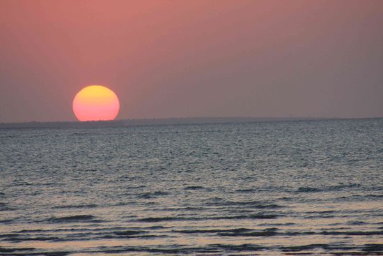 Die Sonne scheint zum Sonnenuntergang riesig zu sein und blutrot.