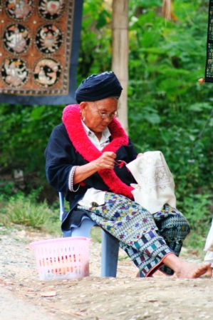 eine Frau im traditionellen Gewand, hier ein paar infos zu den Yao Dörfern
Ihre Häuser sind ebenerdig und werden aus Holz errichtet.
Die Frauen der Yao sind bekannt für ihre wunderschönen Stickereiarbeiten (was die Frau hier gerade macht, man kann natürlich auch alles kaufen)
Die Bestandteile ihrer Tracht wird aus schwarzem oder indigoblauem Baumwollstoff gemacht und besteht aus Hosen, Überkleid, Schärpe und Turban. In erster Linie der schwarze Turban und die mit roter Wolle geknüpfte Schärpe fallen auf.