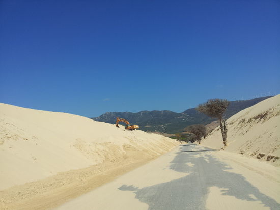 der Bagger sorgt dafür, das die Straße frei von Sand bleibt