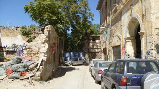 Müll und Ruinen, dahinter ist die Grenze mit angemalten Tonnen und Zäunen  verbarikadiert.