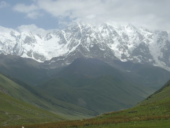 Der Abschluss des weitläufigen grünen Tals wird durch über 5.000 m hohe vergletscherte Berge gebildet. Der Hauptkamm des Großen Kaukasus bildet hier die Grenze zu Russland.