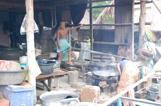 Der Mann drückt die Masse durch das Sieb mit seinem Körpergewicht, wenn man genau hinsieht, sieht man rechts die Nudeln in den Kochtopf fallen