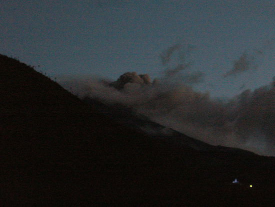 Graue Rauchwolken steigen aus dem ueber 5000 m hohen Tungurahua. Rechts an der Flanke blau beleuchtet: Mirador de la Virgen.