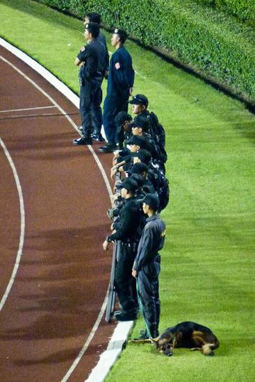 Dem Hund war das Speil zu langweilig. Die Polizei darf in Thailand den Match schauen und steht mit dem Rücken zu den Fans