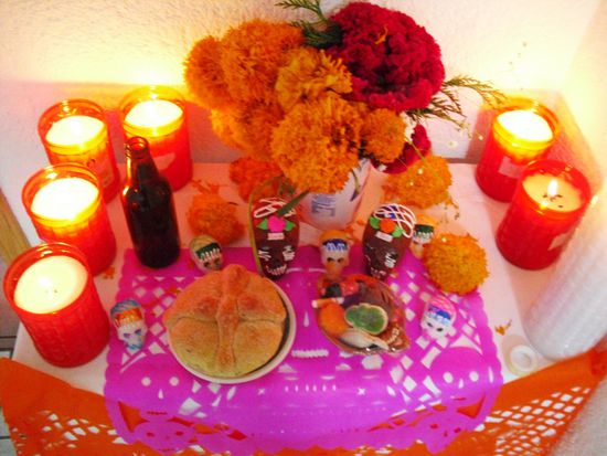 Ok, das hier ist ein Altar. 
An der Wand dahinter hängen Bilder der Verstorbenen. Eine rote Kerze für jeden (mit Namen darauf). Die große, weisse Kerze rechts ist für alle anderen "Seelen". Die Kerzen sollen den Weg erleuchten vom Himmel zum Altar damit der Tote sich nicht verirrt. Die Blumen sollen ebenfalls helfen den Weg zu finden nach dem Motto "immer der Nase nach". Bier und ähnliche Dinge sind Lebensmittel, die der Tote zu Lebtag gern getrunken hat. Es steht geöffnet auf dem Tisch damit der Tote ungehindert trinken kann. Das Brot ist süss und ist ebenfalls ein Genußmittel. Die Totenköpfe sind aus Schokolade oder Marzipan mit den Namen aller Toten, deren gedacht wird. Vor dem Altar liegt ein Teppich, auf dem der Tote schlafen kann und sich ausruhen vom langen Weg vom Himmel zum Altar. Ein schöner Brauch, der tatsächlich so oder ähnlich in jedem Haushalt zu finden ist.