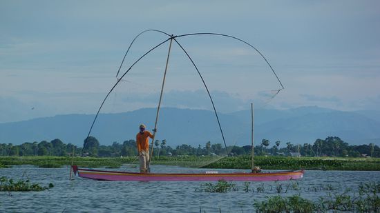 Fischer auf dem See. Zwischen den vier gebogenen Stäben ist ein Netz gespannt, das unter Wasser getaucht wird.