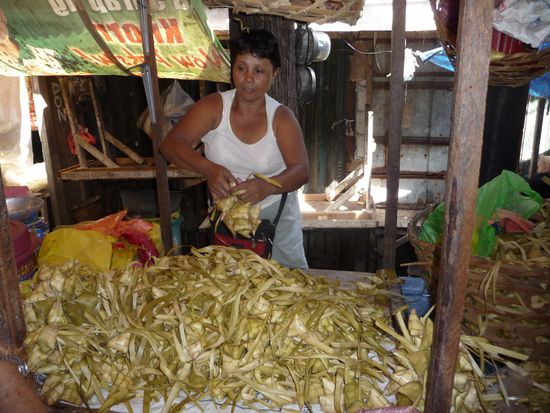 Hier werden aus Kokosblattstreifen kleine Körbchen geflochten und später mit Reis gefüllt und gekocht. Diese Päckchen finden wir abends in den Garküchen wieder.