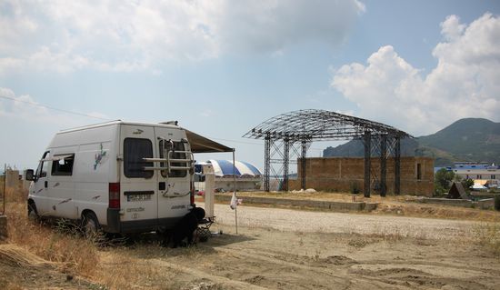 Unser Stellplatz in Koktebel mit einer ganz besonderen Aussicht - vorne eine nicht fertiggestellte Bühne, links daneben mit blau-weißem Dach das Delphinarium und im Hintergrund die Berge
