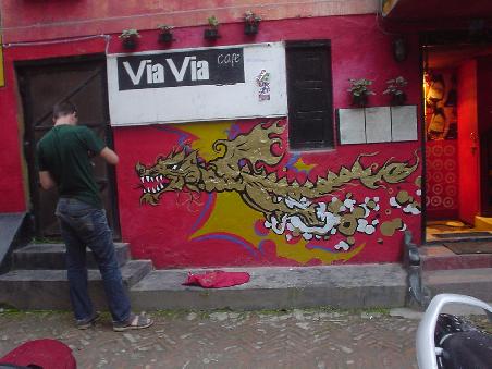 Aaron malt einen Drachen im Cafe Via Via in Kathmandu an die Eingangstuer.