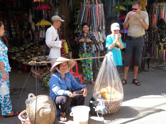Am Markt von Chau Doc. Chris und Carlo sind mutig und probieren ein neues Gebaeck, süss und fettig, aber schmeckt gut.