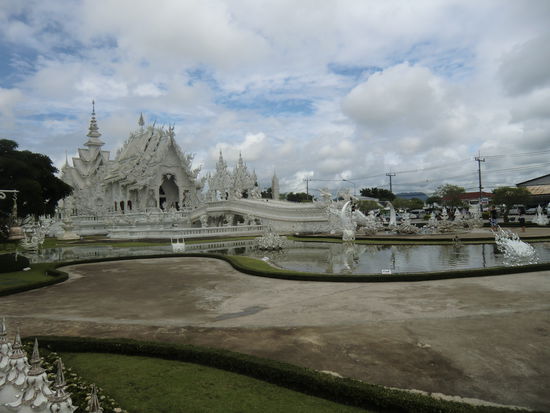 noch einmal eine Gesamtansicht der Anlage.
Da der Wettergott mit uns Erbarmen hatte, war inzwischen die Sonne raus gekommen.
Das hatte zur Folge, dass wir ohne Sonnenbrille gar nichts mehr gesehen haben.
Die gesamte Tempelanlage ist, wie man sieht, in weiß gehalten und mit kleinen Spiegeln verziert.
Somit hat man bei Sonnenschein eine Helligkeit, die unglaublich ist.
Wir sind froh, dass die Bilder gut geworden sind.
Wer noch bessere sehen möchte, der müsste dann mal bitte googeln.
Im Innern des Tempels ist das Fotografieren leider verboten. Der Künstler hat unglaubliche Arbeit geleistet. 
Alle Wände sind mit kleinen Figuren ( von Badman, Spiderman, Michael Jackson, Buddas und vielem Anderen ) bemalt.
Unmöglich, das zu beschreiben !!!!
Es finden sich noch einige Nebengebäude mit Ausstellung und natürlich Souvenirshops, die ebenfalls vom Künstler gestaltet wurden.