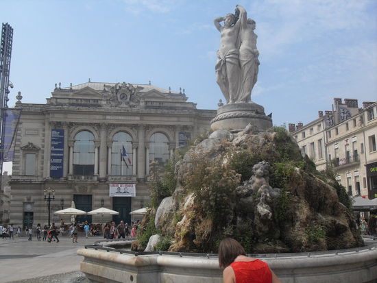 Doro vor dem Brunnen der drei Frauen sowie im Hintergrund das Theater