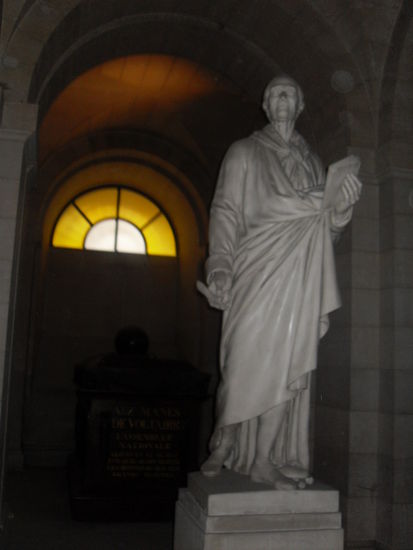 Eine Status Voltaires und im Hintergrund sein Sarkophag