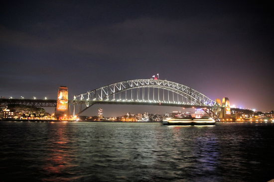 Bei diesem schönen nächtlichem Anblick der Harbour Bridge hörten wir aber zuerst die Vorband. Das Schiff im Bild (unterhalb der Brücke) ist übrigens die Fähre nach Manly. Die Pfeiler der Brücke wurden aus aktuellem Anlass mit Bildern und Sprüchen von Saint Mary MacKillop (erste australische Heilige) angestrahlt, die am folgenden Wochenende in Rom heilig gesprochen wurde.