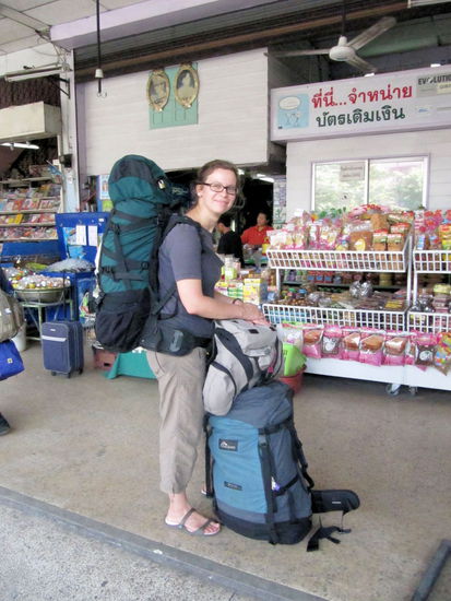 Lizzy mit all unseren Habseligkeiten am Busbahnhof in Chiang Mai. Über Lizzys Kopf/Rucksack sieht man die typischen Bilder vom König bzw. Königsfamilie. In diesem Fall Bilder des Königs und der Königin in jung.