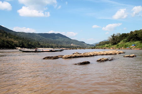 Häufig müssen Felsen im Fluss umfahren werden. Obwohl einige Laoten auf unserem slowboat mitgefahren sind, gibt es einige, die in kleineren slowboats (links im Bild) unterwegs sind, oder in ...