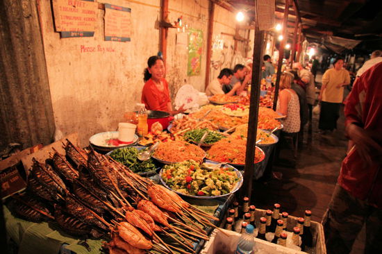 Von Kuchen und Süßspeisen mal abgesehen, haben wir abends meist vegetarisch gegessen. In einer kleinen Gasse neben dem Ancient Luang Prabang Hotel gibt es viele Stände, die leckeres Essen anbieten. Die Basis bildet das vegetarische Buffet (Bildmitte) für unschlagbare 10.000 Kip (weniger als 1 Euro). Man erhält einen leeren Teller und kann ihn am Buffet mit den unterschiedlichsten vegetarischen Speisen befüllen. Hat man den Teller vollgeladen, wird alles zusammen im Wok kurz erhitzt. Danach setzt man sich in den zum Stand gehörenden Sitzbereich (hinter dem Buffet zu erkennen). Sollte einen die vegetarische Kost nicht befriedigen, kann das Mahl mit Fisch oder Fleischspießen (vorne links - gegen Aufpreis) aufgepeppt werden. Selbstverständlich sind auch gekühltes Bier und Softdrinks (am unteren Bildrand) erhältlich. Uns hat aber immer das super leckere und günstige vegetarische Buffet ausgereicht.