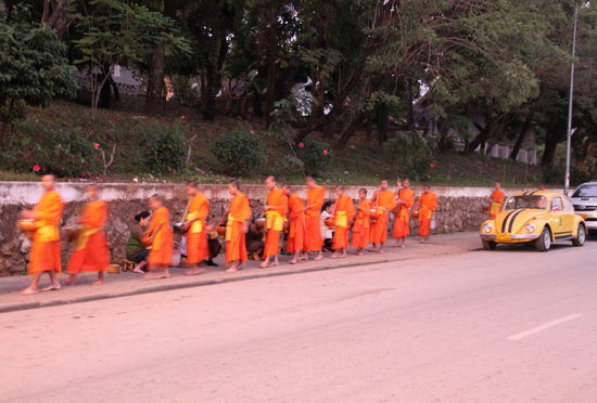 Nach einiger Zeit kamen die ersten Mönche. Jeden Morgen strömen die Mönche bei ihrem Almosen- oder Bettelgang aus den Klöstern/Tempelanlagen um sich ihr Essen abzuholen. Die Mönche gehen in Gruppen die Straßen entlang und sammeln mit ihren Gefäßen Essen ein. Toll ist auch der alte Käfer rechts im Bild. 
Dies und die folgenden Mönchsbilder sind teilweise etwas unscharf, da es noch recht dämmerig war und ich keinen Blitz benutzen wollte.