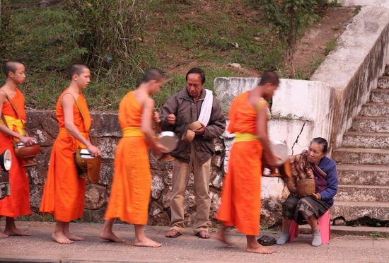 Der Mönch (barfuss) nimmt den Deckel von seinem Essgefäß ab und der Schenkende kann das Essen (meistens Klebreis) in das Gefäß geben.