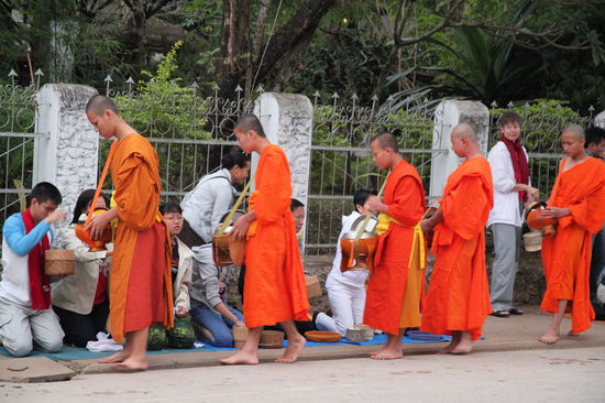 Wobei das Ganze kein Betteln der Mönche darstellt. Der Mönch bedankt sich nicht für die Essensgabe, sondern die Person (häufig kniend), die dem Mönch das Essen gibt bedankt sich beim Mönch. Durch das Beschenken des Mönches verbessert sich nämlich das Kharma des Schenkenden. Es gesellen sich auch Touristen zu denen, die den Mönchen Essen geben. Man kann Klebreis kaufen um sich an der Essensübergabe zu beteiligen.