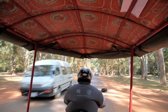 Unser Fahrer/Tuk Tuk auf einer Straße innerhalb von Angkor Thom. Da der Weltkulturerbepark Angkor Wat etwas außerhalb der Stadt Siem Reap liegt und die einzelnen Tempel auch nicht wirklich nah beieinander stehen, ist ein eigenes Tuk Tuk mit Fahrer eine bequeme Fortbewegungsmöglichkeit.