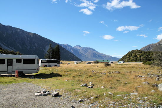 Morgens auf dem DOC-Campingplatz 'White Horse Hill' direkt am Fuße der gewaltigen Berge. Blick Richtung Tal / Lake Pukaki. Die große Hütte mit dem grünen Dach ist Toilettenblock und Aufenthaltsraum. Wir hatten großes Glück mit dem Wetter und strahlenden Sonnenschein.