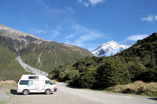 Wir standen am nördlichen Ende des Platzes, wo es versteckt zwischen den Bäumen noch einen weiteren Toilettenblock gab. Alle Einrichtungen waren ganz neu und es gab saubere Klos mit Wasserspülung (und Toilettenpapier) sowie Waschbecken (ohne Seife).
Der Berg im Hintergrund ist noch nicht der Aoraki / Mount Cook!