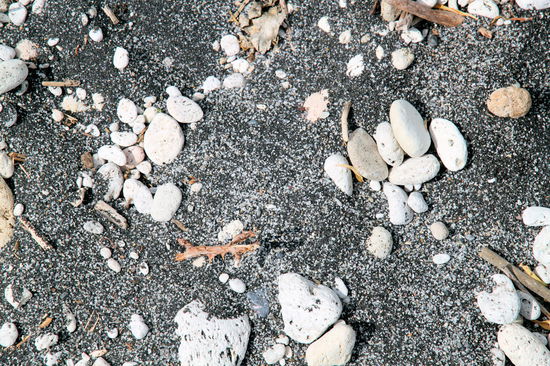 Am Ufer finden sich unterschiedliche Sandfarben, von hell bis sehr dunkel. Die kieselartigen Steine sind Bimssteine und damit Überbleibsel vom Vulkan. Die 'Steine' sind super leicht und eignen sich gut zur Fußpflege. 