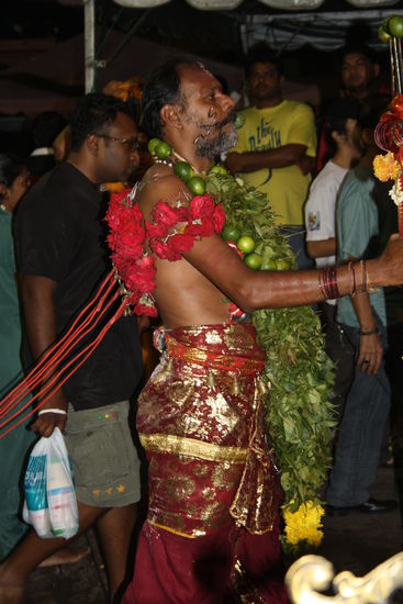 Haken mit Rosen am Rücken. Zusätzlich größere Haken an denen ein Wagen hängt, den er viele Kilometer barfuß hinter sich her zieht.