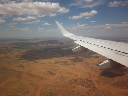 Heute in dunkelrot, hinter dem Wolkenschatten sieht man den Ayers Rock, der bei jedem Wetter in einer anderen erdigen Farbe erstrahlt.