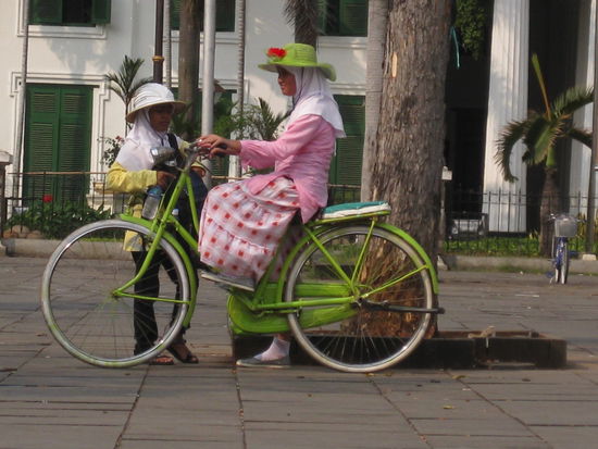 durch die jahrhundertelange hollaendische Kolonialherrschaft gibt es noch einige Reliquien wie "Holland-Fahrraeder" und den passenden "Damen-Hut" aus der Zeit und in diesem Fall erfreuen sich muslimische Indonesinnen an dem hier ungewoehnlichen Fortbewegungsmittel