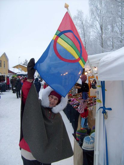 Christa mit ihrem neuen Poncho an einem Stand mit Sameflagga.