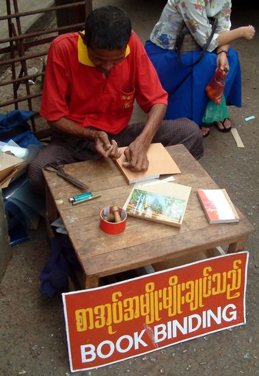 Buchbinder am Straßenrand. Es wird viel gelesen in Myanmar, die Alphabetisierungsrate liegt bei über 90%, Fernseher hingegen sind noch Luxusartikel.