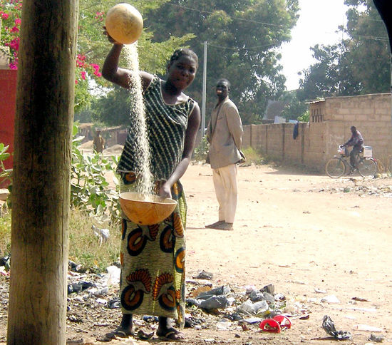 Fatoumata beim Schleudern von Hirsekörnern zur Reinigung vor dem Haus