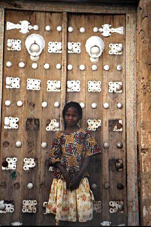 Ein Mädchen namens Aisha vor einer typischen Türe in Timbuktu