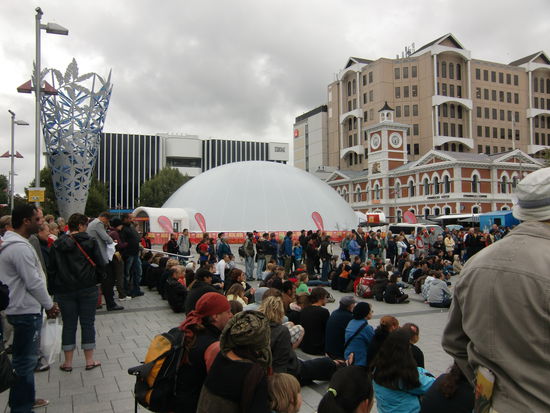 Das Buskerpublikum auf dem zentralen Platz in Christchurch mit Lichtskulptur links und dem Buskerzelt fuer die Abendveranstaltungen.