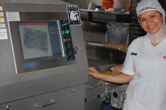 Die Qualitätskontrollmaschine mit der Qualitätskontrollmaschinenbedienerin (gleichzeitig Abteilungsleiterin). Kleinste Häärchen werden mittels Röntgenstrahlen erfasst. Solcherlei fehlerhaftes Produkt wird sofort mittels Luftstrahl vom Fließband katapultiert!