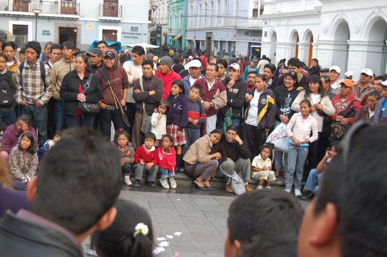Viele Ecuadorianische Gesichter, die begeistert einem Strassenkuenstler zuschaun.