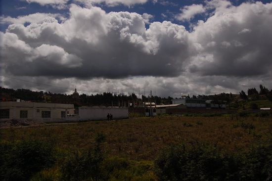 Andenlandschaft mit Wolken vor stahlblauem Himmel. Irgendwo hinter den Wolken versteckt sich der Chimborazo, mit 6.310 Metern höchster Berg Ecuadors.