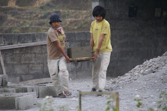 Zwei Jungen tragen einen frischen Mauerstein