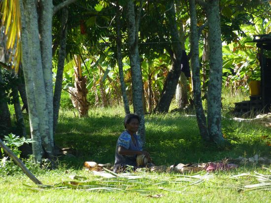 Frau im Schatten beim Rollen trockener Palmenblätter