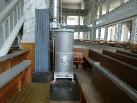Im Innern der Kirche mit Kanonenofen, die Sitzhöhe der Bänke ist zu beachten