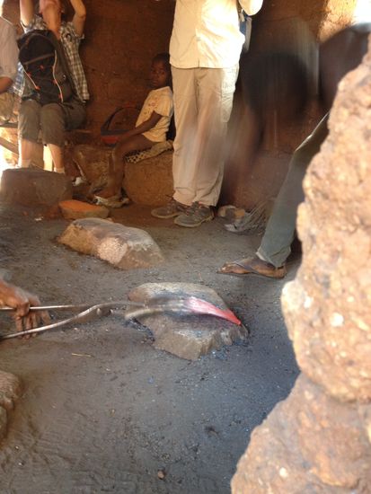 Mit einem Stein wird das glühende Eisen bearbeitet. Das ist nur schwer aufs Bild zu bringen, bei der Geschwindigkeit, mit der der junge Mann vorgeht